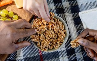 3 hands taking walnuts from a bowl on a picnic blanket